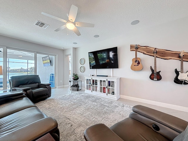 living room featuring tile patterned floors, visible vents, a ceiling fan, a textured ceiling, and baseboards