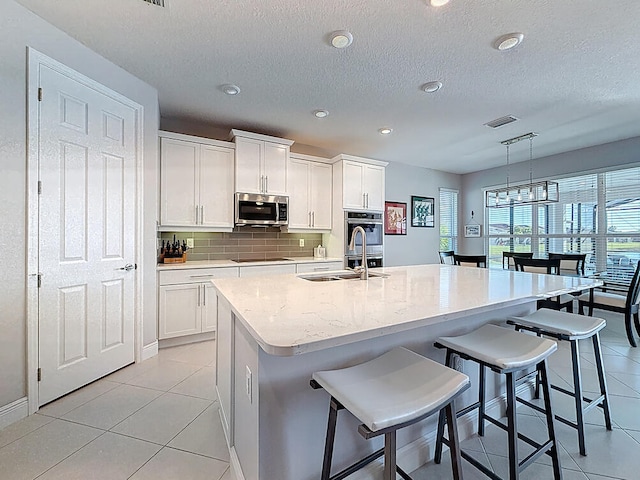 kitchen with visible vents, a sink, decorative backsplash, appliances with stainless steel finishes, and white cabinetry