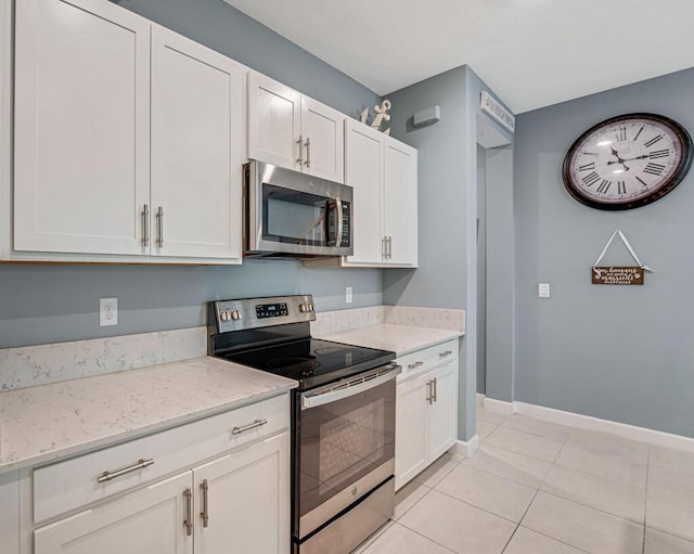 1012 Willow Pl, Riviera Beach, FL 33410 - kitchen with appliances with stainless steel finishes, white cabinetry, light tile patterned floors, light stone counters, and baseboards