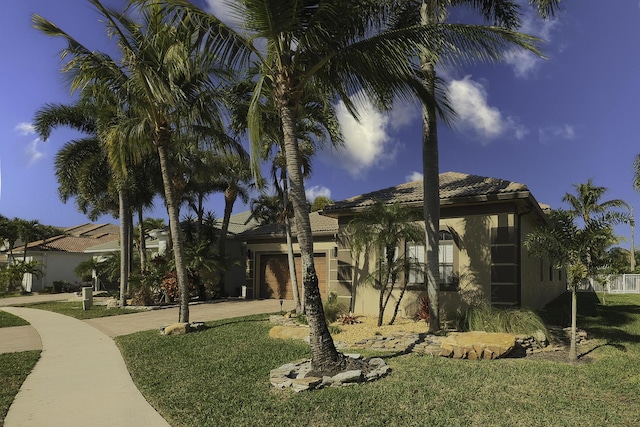 view of property exterior featuring a tiled roof, stucco siding, a lawn, a garage, and driveway