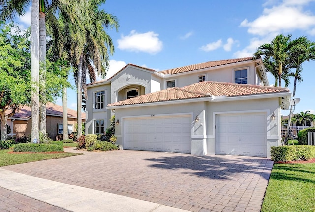 mediterranean / spanish house featuring stucco siding, decorative driveway, a tiled roof, and a garage