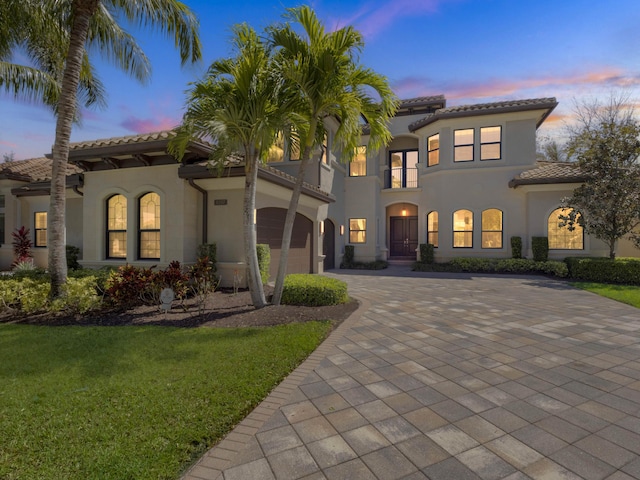 mediterranean / spanish home featuring stucco siding, decorative driveway, an attached garage, a front yard, and a tiled roof