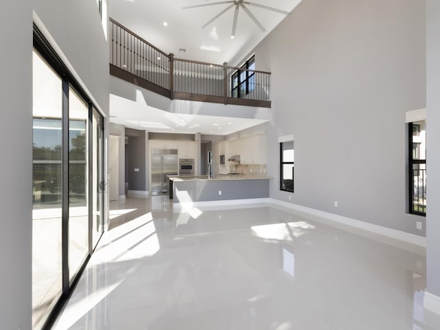 unfurnished living room featuring a ceiling fan, a high ceiling, a healthy amount of sunlight, and baseboards