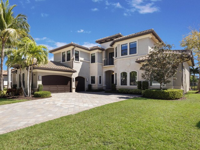 mediterranean / spanish home featuring stucco siding, a front lawn, decorative driveway, an attached garage, and a tiled roof