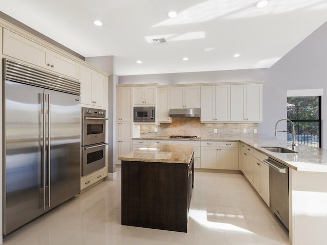 kitchen featuring visible vents, a sink, decorative backsplash, under cabinet range hood, and built in appliances
