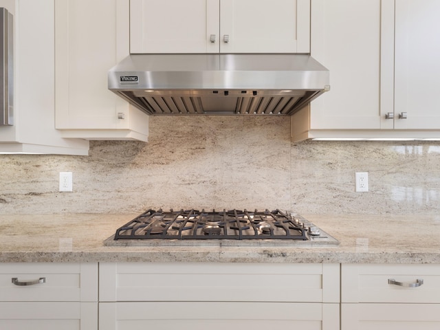 kitchen featuring tasteful backsplash, ventilation hood, stainless steel gas cooktop, light stone counters, and white cabinetry