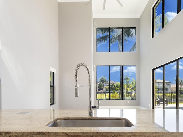 kitchen with a high ceiling, stone countertops, ceiling fan, a sink, and crown molding