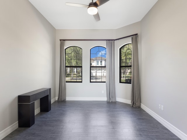 empty room with baseboards, dark wood-type flooring, and a ceiling fan