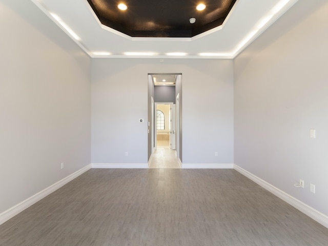empty room featuring baseboards, a raised ceiling, and wood finished floors