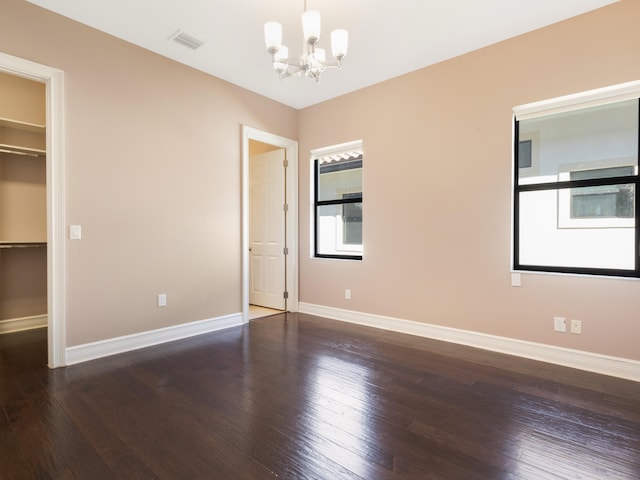 unfurnished bedroom featuring visible vents, baseboards, wood-type flooring, a walk in closet, and a chandelier