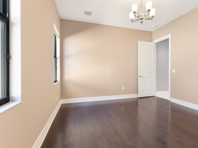 empty room featuring a notable chandelier, visible vents, baseboards, and wood finished floors