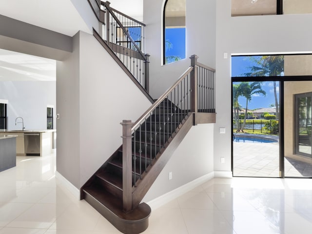 stairway with tile patterned flooring, baseboards, and a towering ceiling