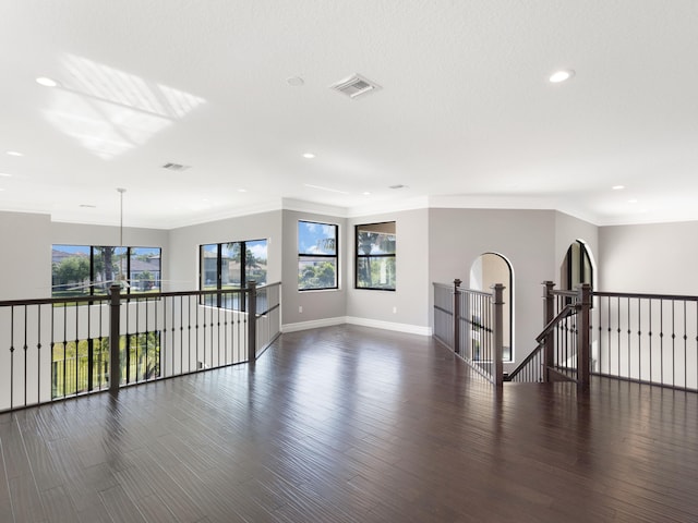 empty room featuring visible vents, baseboards, dark wood-style floors, and crown molding