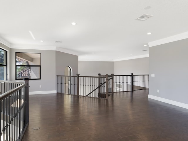 empty room with crown molding, wood finished floors, baseboards, and visible vents