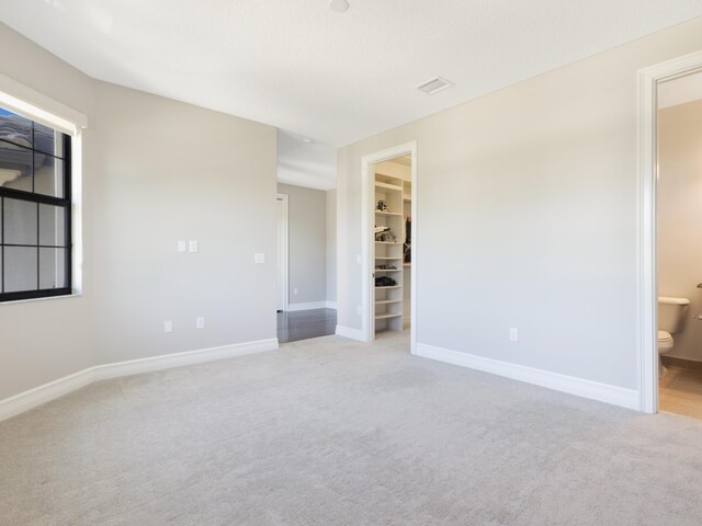 unfurnished bedroom featuring ensuite bath, a closet, baseboards, light colored carpet, and a spacious closet