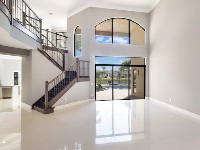 tiled foyer entrance featuring stairway, crown molding, baseboards, and a towering ceiling