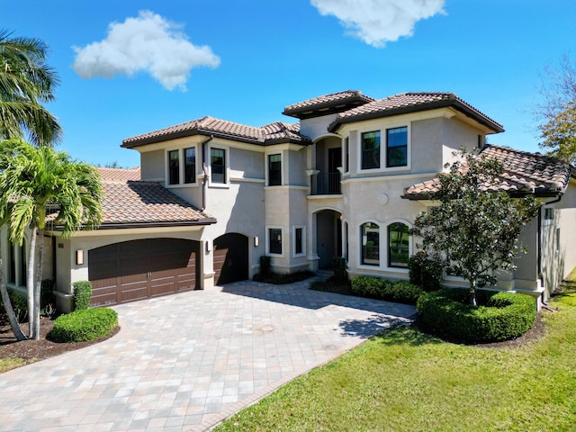mediterranean / spanish-style home featuring stucco siding, a tile roof, decorative driveway, and a garage
