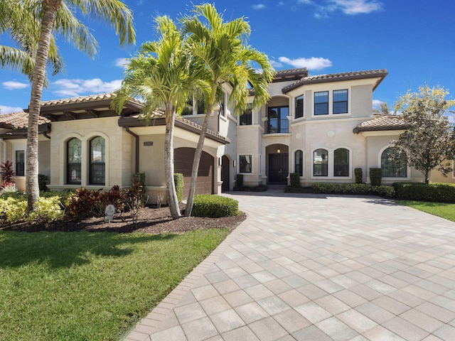 mediterranean / spanish house featuring a tiled roof, decorative driveway, a garage, and stucco siding