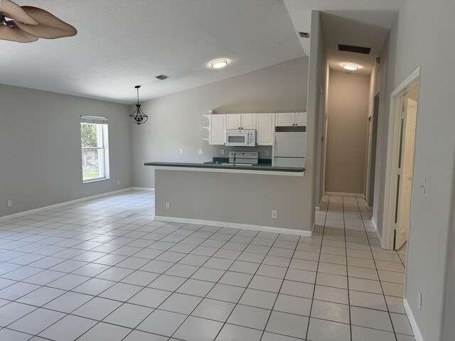 kitchen with white appliances, dark countertops, white cabinetry, light tile patterned floors, and hanging light fixtures