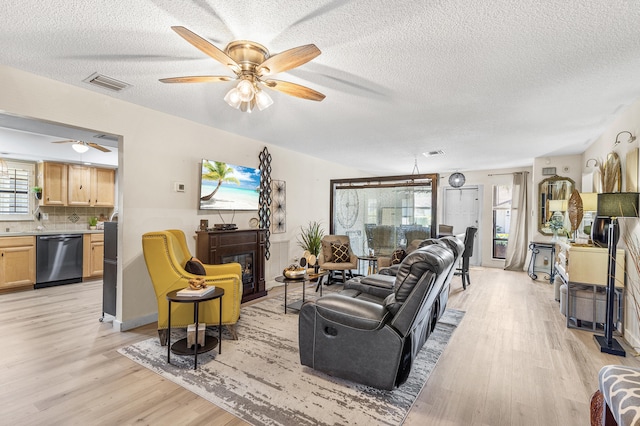 living area with a glass covered fireplace, light wood-style floors, visible vents, and ceiling fan
