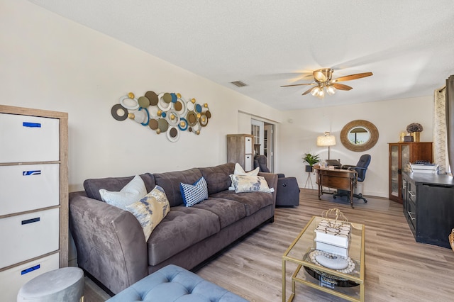 living room with visible vents, light wood-style floors, ceiling fan, and a textured ceiling