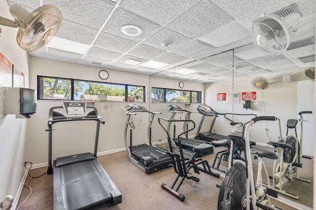 workout area featuring baseboards, a paneled ceiling, and a healthy amount of sunlight