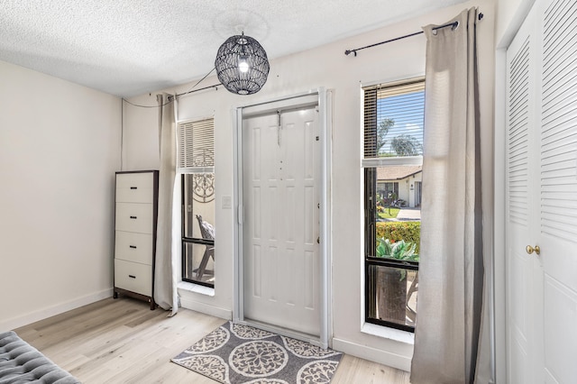 foyer entrance featuring baseboards, a textured ceiling, and light wood finished floors
