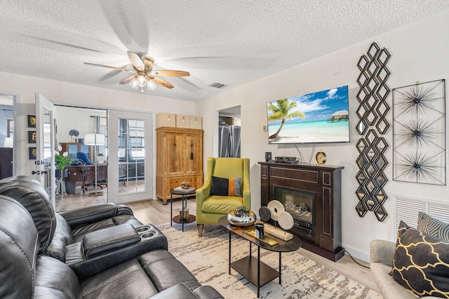 living area with visible vents, a textured ceiling, a ceiling fan, and light wood-style floors