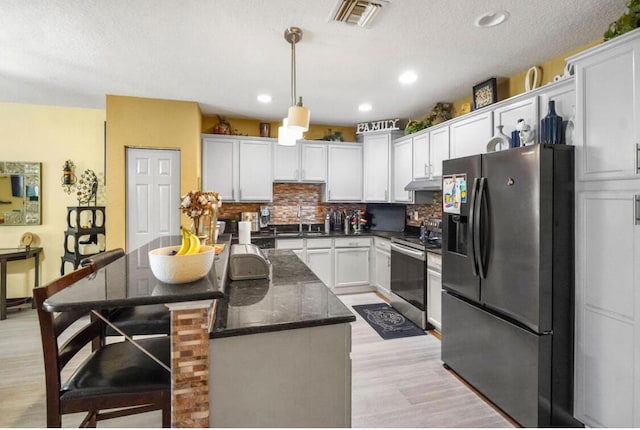kitchen featuring visible vents, decorative backsplash, electric stove, black fridge with ice dispenser, and under cabinet range hood