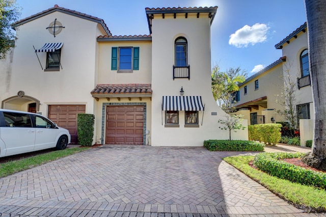 mediterranean / spanish-style home with decorative driveway, a tiled roof, an attached garage, and stucco siding