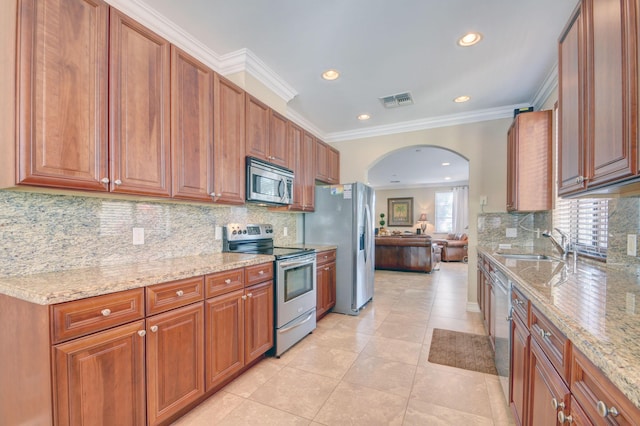 kitchen with visible vents, light stone counters, appliances with stainless steel finishes, arched walkways, and a sink