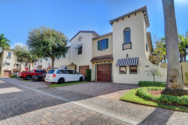 view of front of home with decorative driveway, a garage, stucco siding, and a tiled roof