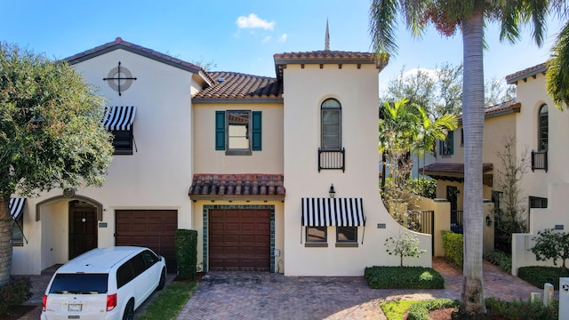 mediterranean / spanish house featuring decorative driveway, stucco siding, an attached garage, and a tiled roof