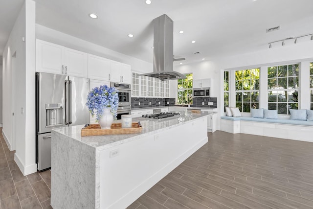 kitchen with island exhaust hood, a kitchen island, light stone countertops, visible vents, and appliances with stainless steel finishes
