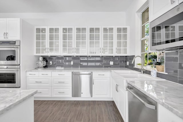 kitchen with stainless steel appliances, tasteful backsplash, glass insert cabinets, and a sink