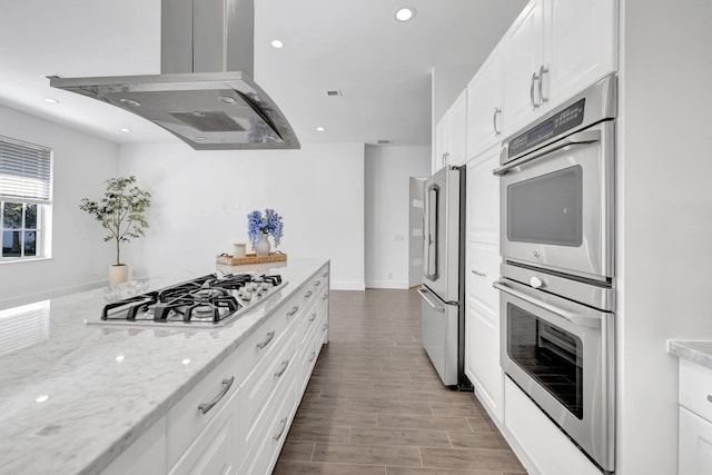 kitchen with white cabinets, appliances with stainless steel finishes, island exhaust hood, wood finished floors, and light stone countertops