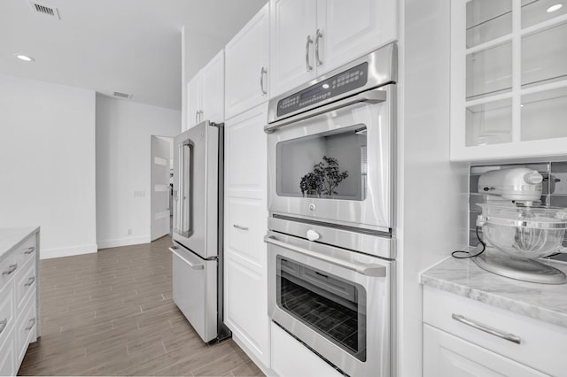 kitchen featuring light wood-type flooring, white cabinetry, high quality fridge, and double oven