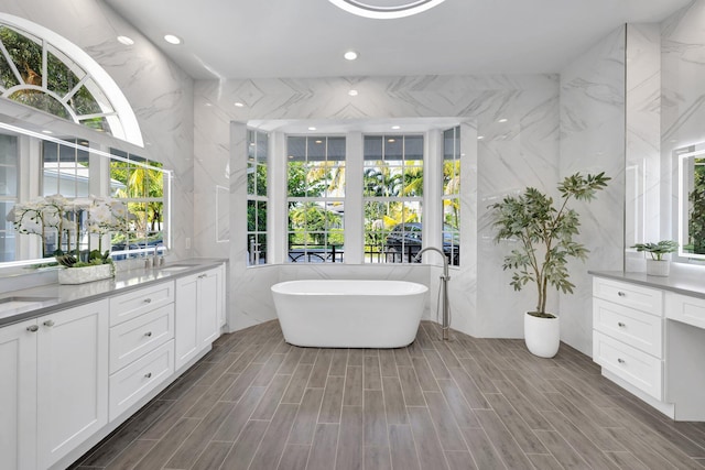 bathroom with a sink, double vanity, a freestanding tub, and plenty of natural light
