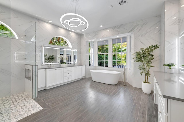 full bath with a freestanding tub, visible vents, a sink, a marble finish shower, and double vanity