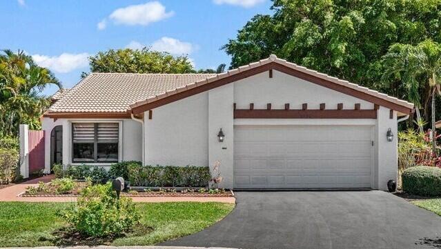 mediterranean / spanish-style home featuring a tiled roof, stucco siding, an attached garage, and aphalt driveway