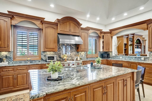 kitchen featuring ventilation hood, black microwave, light stone counters, and a healthy amount of sunlight