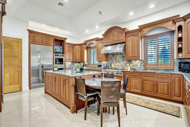 kitchen with range hood, visible vents, a kitchen island with sink, stainless steel appliances, and light stone counters