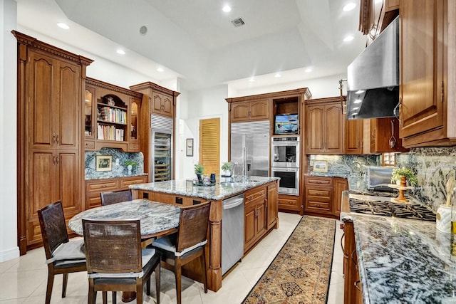kitchen with an island with sink, exhaust hood, visible vents, appliances with stainless steel finishes, and light stone counters