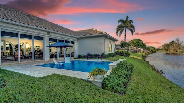 pool with a patio, a yard, and a water view