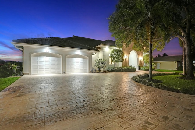 mediterranean / spanish-style house featuring a tiled roof, a garage, stucco siding, and decorative driveway