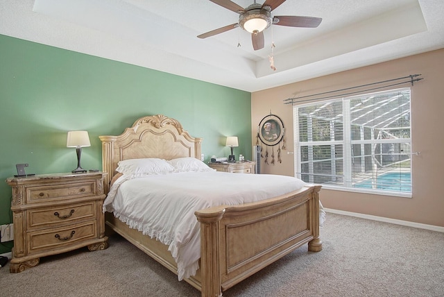 bedroom with baseboards, a raised ceiling, light colored carpet, and a ceiling fan