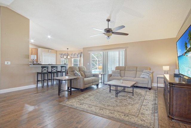 living area with baseboards, wood finished floors, ceiling fan, and vaulted ceiling