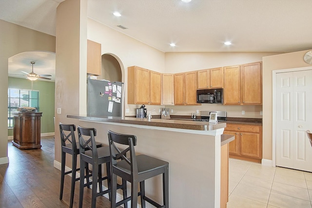 kitchen featuring lofted ceiling, freestanding refrigerator, stove, black microwave, and a kitchen bar