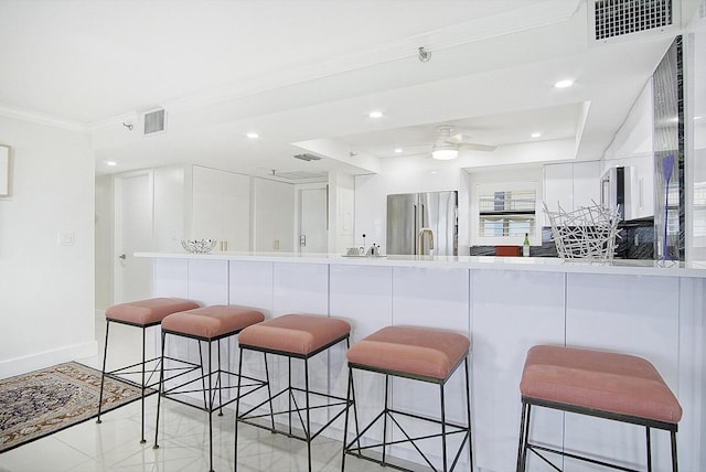 kitchen featuring a kitchen bar, ornamental molding, stainless steel fridge, and visible vents