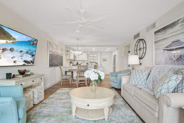 living area with ceiling fan with notable chandelier, visible vents, wood finished floors, and baseboards